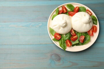 Delicious burrata cheese with tomatoes and basil on light blue wooden table, top view. Space for text