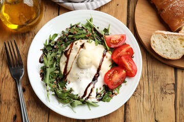 Delicious burrata cheese with arugula, tomatoes and dressing on wooden table, flat lay