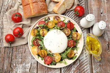 Delicious burrata cheese with arugula, tomatoes and dressing on wooden table, flat lay