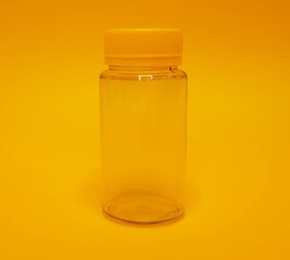 Transparent plastic jar with a yellow lid on a yellow background, empty, cylindrical shape, without label, subject shooting, space for text.