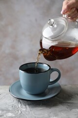 Woman pouring hot tea into cup from teapot at grey table, closeup