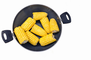 Bright yellow boiled corn cobs halves in a pot, viewed from directly above on white background