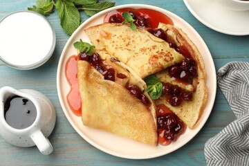 Delicious crepes with cherry jam served on light wooden table, flat lay