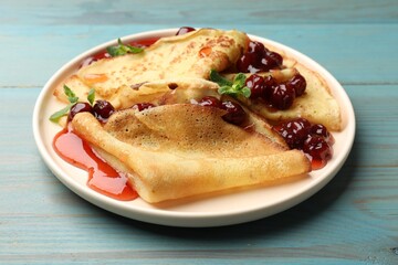 Delicious crepes served with cherry jam on light blue wooden table, closeup