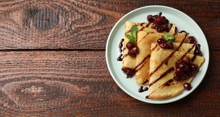 Delicious crepes with cherry jam and chocolate on wooden table, top view. Space for text