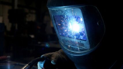 Welder man working close up. Close up view of metal welding process with sparks and bright light. Industrial worker with safety mask.