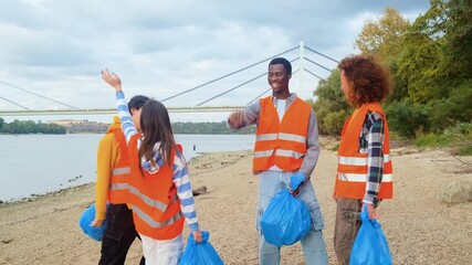 Portrait of a group of volunteers standing on the riverbank celebrating with their hands up after collecting plastic waste.