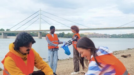 Smiling volunteers collecting garbage in blue bags during riverbank cleanup. - Powered by Adobe