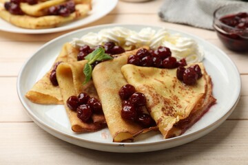 Tasty crepes with cherries, whipped cream and mint served on white wooden table, closeup