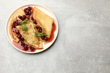 Tasty crepes with cherries, jam and mint on light table, top view. Space for text