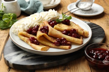 Tasty crepes with cherries, whipped cream and mint served on wooden table, closeup