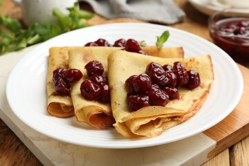 Tasty crepes with cherries and mint served on wooden table, closeup
