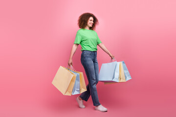 Young woman wearing a green tshirt walks with pastel shopping bags against a pink background showing joy style and shopping energy
