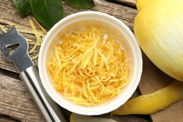 Bowl with lemon zest, fresh fruit, leaves and zester on wooden table, flat lay