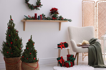 Stylish room with small spruce trees, armchair and Christmas decor. Interior design