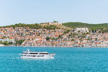 The coastal town of &Scaron;ibenik in Croatia sits on the seafront, with hilltop houses, the Barone Fortress, and St. Michael's Castle. View from the other side on a sunny summer day.