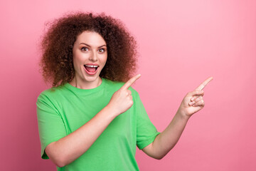 Happy young woman with curly hair in a green tshirt points to the sides against a pink background for lifestyle advertising and fashion use
