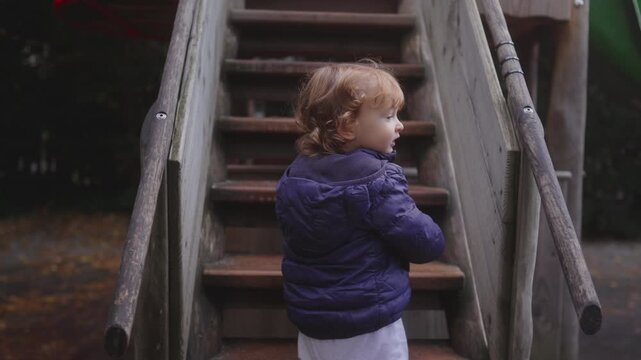 Toddler standing at wooden playground stairs preparing to climb while observing surroundings creating natural outdoor moment filled with curiosity early confidence