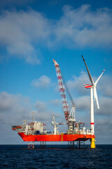 Fototapeta premium Offshore wind farm construction with a heavy-lift jack-up vessel installing a giant turbine. Renewable energy construction, offshore engineering, sustainable power infrastructure