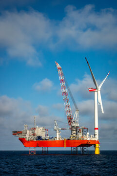 Offshore wind farm construction with a heavy-lift jack-up vessel installing a giant turbine. Renewable energy construction, offshore engineering, sustainable power infrastructure