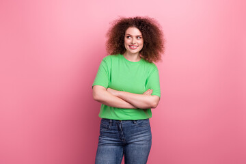 Happy young woman in a green tshirt with curly hair stands against pink background smiling confidently