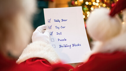 Santa Claus reviewing a handwritten Christmas gift list with checked toy items, wearing white gloves and a red suit, with warm festive lights softly glowing in the background