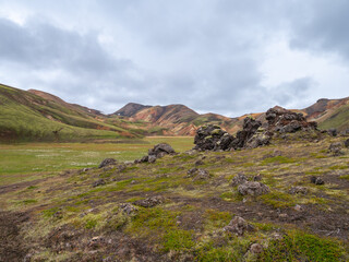 Mossy lava rocks and a green meadow floor lead to the distant, colorful rhyolite mountains in Iceland.