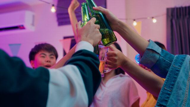 Closeup hands multiethnic young adult Asia friend wear futuristic neon glowing glasses dance and drink alcohol beer fun hangout party in living room night indoor home. Disco lights illuminating house.