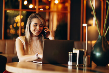 Young business woman working on laptop and talking on the phone in a cafe