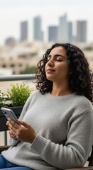 A serene woman with curly hair relaxes on a city balcony with her eyes closed, holding a smartphone.