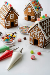 Gingerbread houses decorated with colorful candies and icing, surrounded by piping bags and bowls of sweets, creating a festive holiday atmosphere with copy space