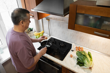 Adult man cracking eggs into frying pan while preparing simple healthy breakfast in home kitchen. Morning Home Cooking Making and Eating Breakfast