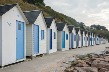 White beach huts with blue doors under cloudy summer sky