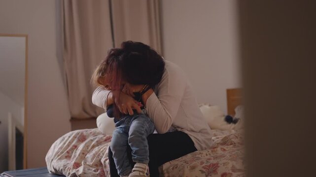 Mother hugging toddler tightly on bed with warm affectionate embrace creating tender comforting moment of closeness love reassurance and gentle connection in relaxed home setting