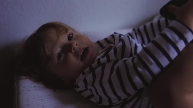 Toddler lying in changing area staring toward camera with calm curiosity creating gentle intimate moment of early awareness and quiet observation in soft indoor setting