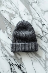 Knitted dark gray woolen headwear rests on a polished white and gray veined stone surface.