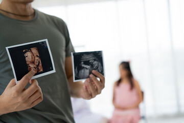 Asian husband hold ultrasound Images of His Unborn Child and pregnant women visit obstetrician for consulting in medical clinics or hospitals planning pregnancy. planning pregnancy, trust and respect