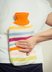 Senior woman with hot water bottle on her back. Help with pain in old age