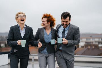 Three business professionals taking a break on the rooftop of a modern office building, chatting and enjoying coffee or tea
