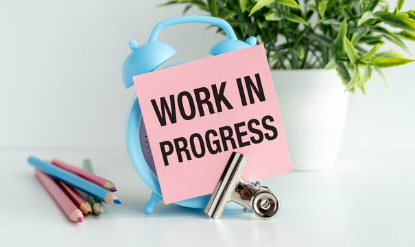 Work in Progress the writing on the sticky note near the blue alarm clock and colored pencils on the table