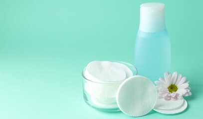 Clean cotton pads, micellar water and flower on turquoise background. Space for text