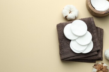Clean cotton pads, flowers and towel on beige background, flat lay. Space for text