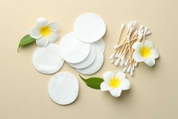 Clean cotton pads, swabs and flowers on beige background, flat lay