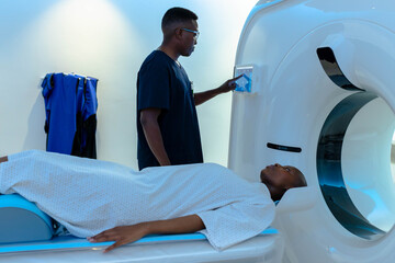 Patient sliding into scanner gantry in radiology room, tech adjusting panel, blue aprons hanging