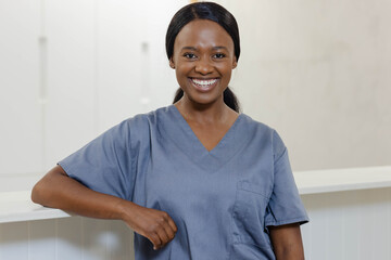 African woman standing behind medical reception desk smiling in gray scrub top with chest pocket