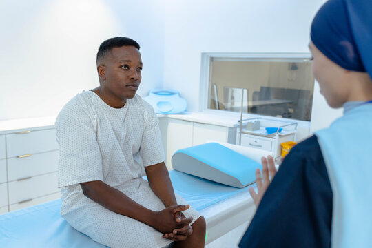 African patient in gown and African clinician in dark scrubs sitting, speaking on exam table sheet