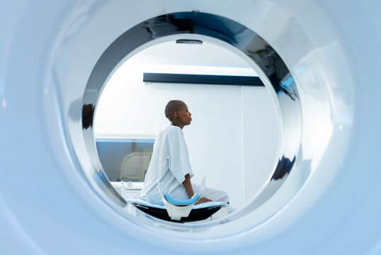 African adult female sitting on scanner table in scanner room, wearing gown and blue headrest