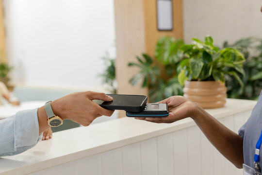 Customer and staff are tapping dark smartphone and card reader on white paneled reception counter