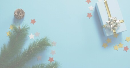 Fototapeta premium Sitting light-blue-gift gold-ribbon silver-bow on pale-blue surface firsprig cone stars, copy space