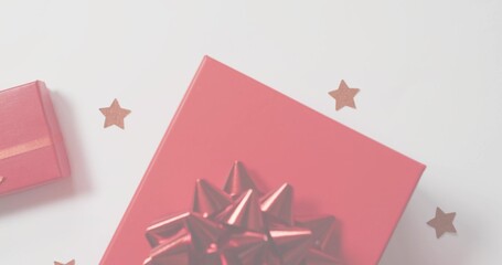 Displaying large red gift box on white table, with shiny bow, small red box, star confetti